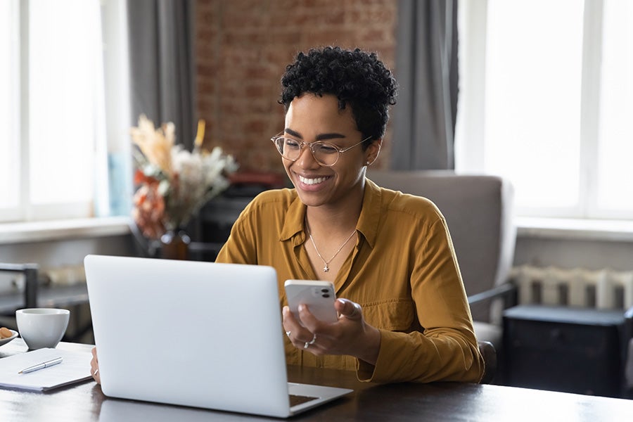 girl looking at the laptop and holding phone in one hand
